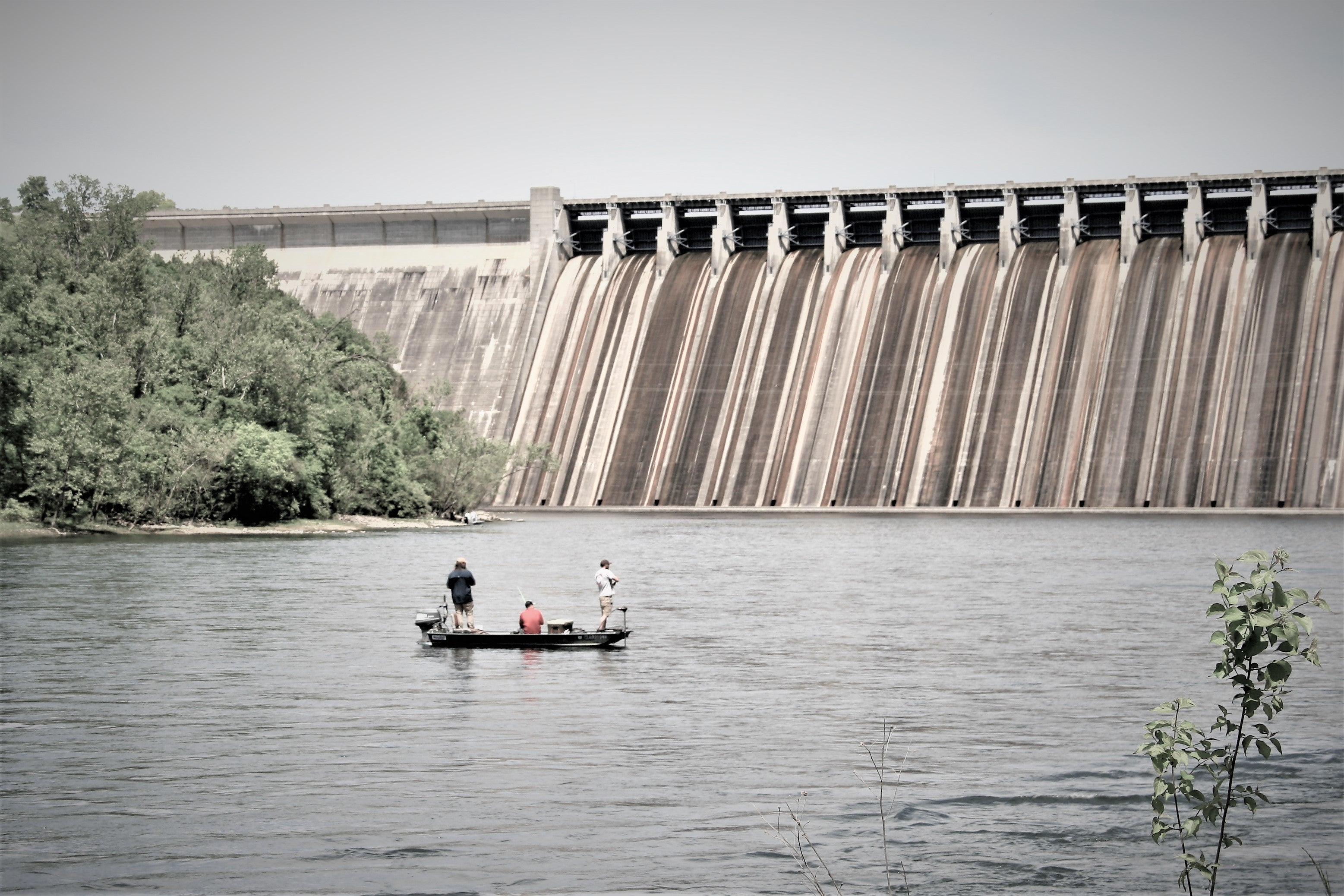 Three people fishing from a riverboat in front of Bull Shoals Dam
